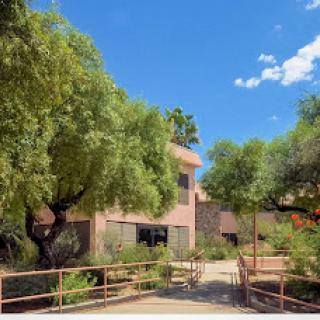 A serene outdoor view featuring a building surrounded by lush greenery and a clear blue sky.