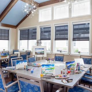 A modern dining room with blue chairs and a set table, illuminated by natural light from large windows.