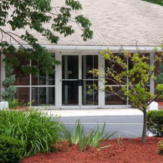 A well-landscaped house with a porch and large windows, surrounded by lush plants and trees.