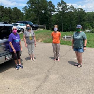 A group of friends gathered outside, practicing social distancing and wearing masks on a sunny day.