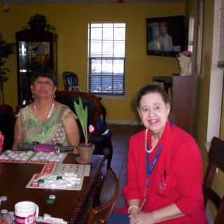 Two people sitting at a table in a room with a window and television.