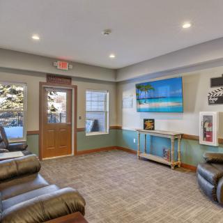 A cozy waiting room featuring leather chairs, a large television, and decorative posters on the walls.