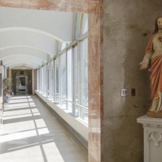 A sunlit corridor featuring a statue alongside large windows.