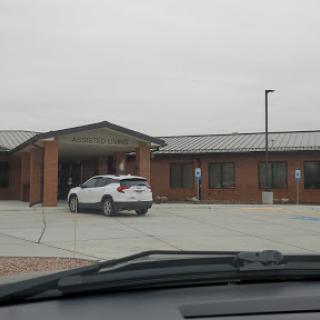 A view of a building with a parked vehicle in the foreground under a cloudy sky.
