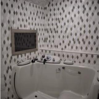 A bathroom with a corner bathtub and patterned tile walls.