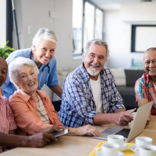 A group of seniors smiling and gathered around a laptop during the day.