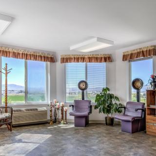 A bright salon waiting room with hairdryer chairs and large windows overlooking a scenic view.