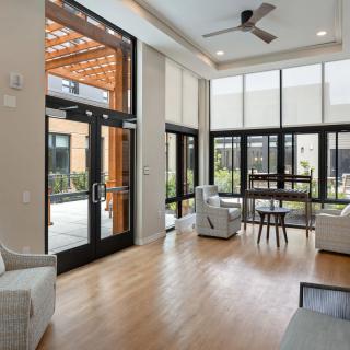 A modern living room with large windows allowing abundant natural light, featuring comfortable furniture and sleek wood flooring.