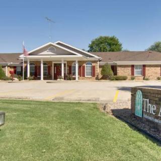 A single-story brick building with a white entrance and green lawn, featuring a sign in the foreground.