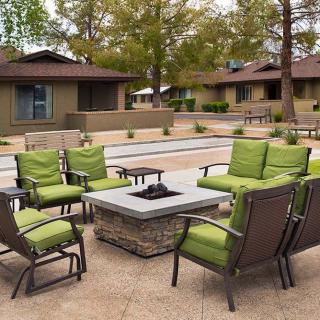 Outdoor patio area with green-cushioned chairs surrounding a fire pit table.