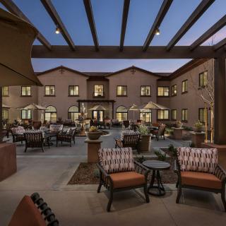 A well-lit courtyard with outdoor seating and a view of a residential building during the evening.