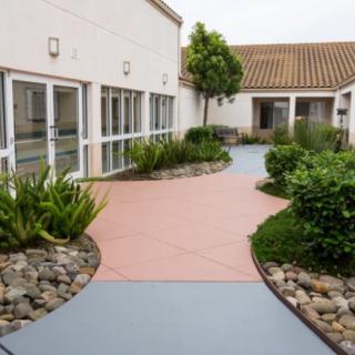 A courtyard with a winding walkway surrounded by landscaped gardens and plants between modern buildings.