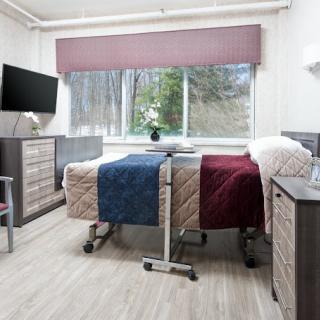 A hospital room with two adjacent beds and a window overlooking the outdoors.