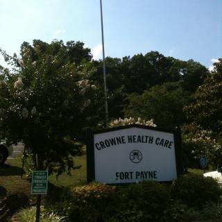 Sign for Crowne Health Care surrounded by trees and shrubs.