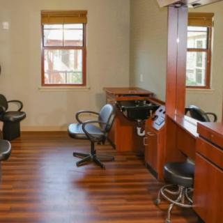 An empty hair salon with chairs and mirrors, featuring wooden flooring and windows.