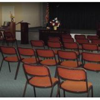 An empty auditorium with rows of chairs facing a podium on stage.