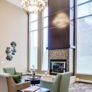 A modern living room featuring a high ceiling, large windows, and a central fireplace with comfortable seating.