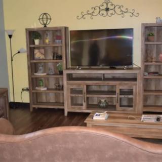 A cozy living room setup with a TV, shelves filled with decor items, and a floor lamp.