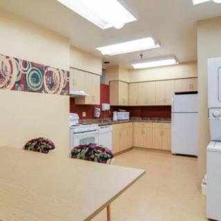 A modern kitchen with wooden cabinets, a refrigerator, oven, microwave, and a dining table with chairs.