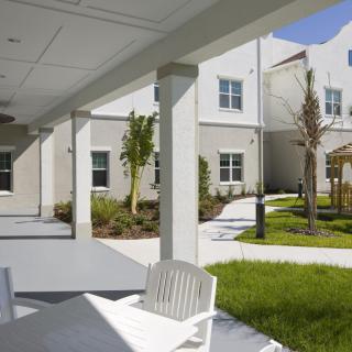 A sunny view of a modern building exterior with a patio area and landscaped lawn.
