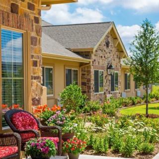 A beautiful garden with colorful flowers and patio furniture in front of a house with a brick exterior.