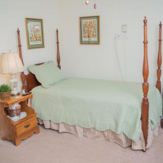 A cozy bedroom with a single four-poster bed, a wooden nightstand, and decorative wall art.