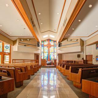 Interior view of a church with wooden pews and colorful stained glass windows.
