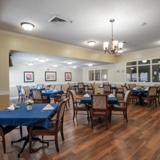 A well-arranged dining area with multiple tables and chairs, featuring a wooden floor and elegant lighting.