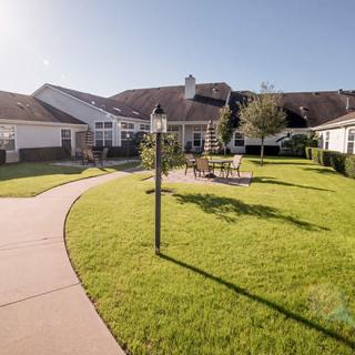A well-maintained garden with a winding pathway, outdoor seating area, and a lamp post on a sunny day.