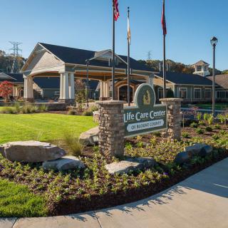 Wide view of a building with a landscaped entrance and flags displayed.