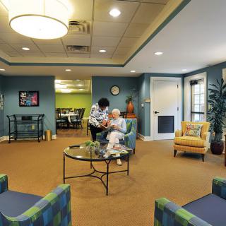 A cozy waiting area in a nursing home with a caregiver attending to an elderly person.