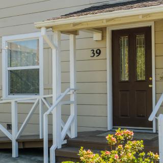 A house entrance with a brown door and the number 39 displayed above, surrounded by a small porch and flowers.