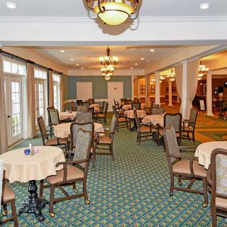 An elegant dining room with neatly arranged tables and chairs, featuring chandeliers and a patterned carpet.