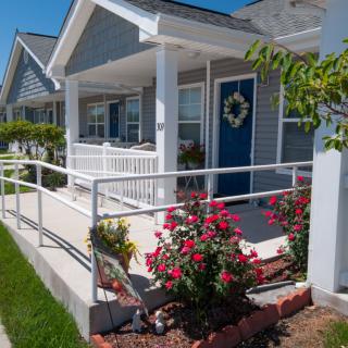 A charming house with a ramp leading to the front porch, decorated with vibrant flowers on a sunny day.
