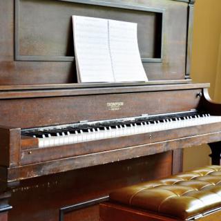 An upright piano with sheet music resting on its stand and a bench in front.