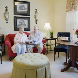 An elderly couple sitting on a red sofa in a cozy living room, engaged in reading.