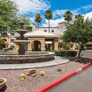 A sunny day at a building entrance with a fountain and desert landscaping.