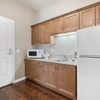 A compact kitchen with wooden cabinets, a microwave, a refrigerator, and a sink.