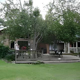 A cozy house with a wooden deck surrounded by lush trees and a green yard.