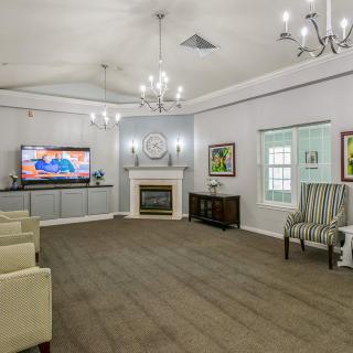 A spacious living room featuring a fireplace, television, and elegant chandeliers with comfortable seating and artwork on the walls.