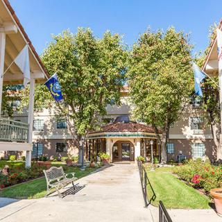 A scenic view of a building entrance surrounded by trees and a well-maintained garden on a sunny day.