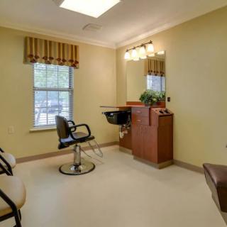 An empty hair salon room with a chair, mirror, and window.