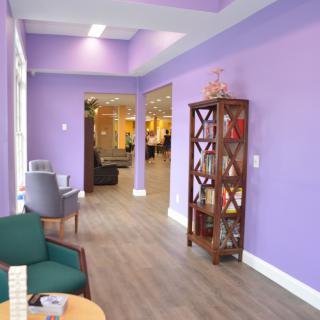 A modern waiting room with purple walls, comfortable seating, and decorative shelving.