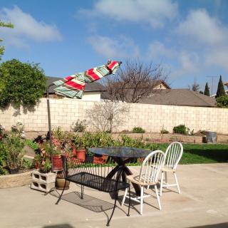 A sunny backyard patio with chairs and an umbrella overlooking a garden.