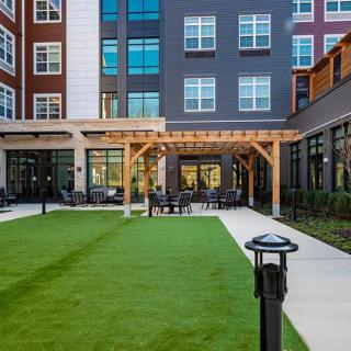 A modern apartment building featuring a well-maintained courtyard with a pergola and lush green lawn.