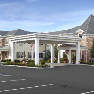 A view of a building entrance with an overhang, surrounded by a parking lot and landscaped areas.