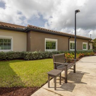 A serene outdoor space with a bench and landscaped garden in front of a building under a cloudy sky.