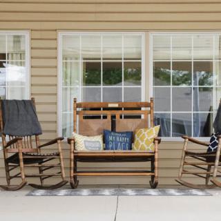 A cozy porch setup with wooden rocking chairs and a swing adorned with colorful cushions.
