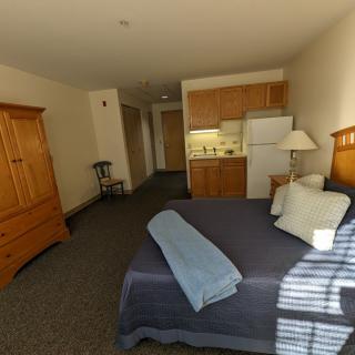 A cozy hotel room with a kitchenette, featuring a neatly made bed and wooden furniture.