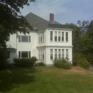 A white residential house surrounded by trees and a lush lawn.